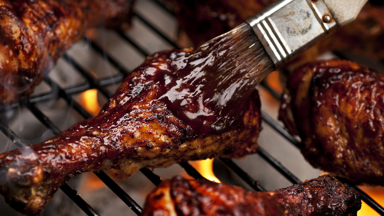 chicken legs on the grill, one of which is being brushed with barbecue sauce