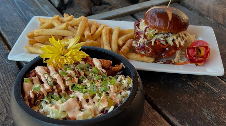 Burger, fries, and chicken bowl decorated with flowers on wooden table