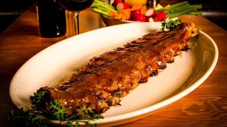 Plated pork ribs smothered in sauce with chopped raw veggies in the background