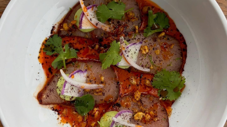 Hamachi crudo with onions and cilantro on white plate