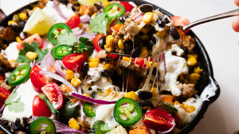 Lifting a spoonful of cheesy turkey and sweet potato skillet