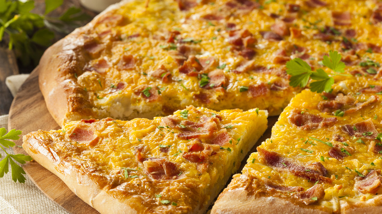 Breakfast pizza with eggs and bacon on a wood board