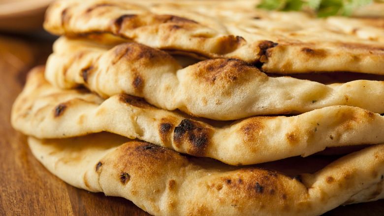 Several cooked naans piled on top of each other on a wooden surface