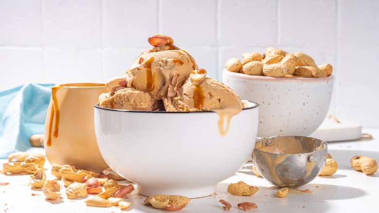 Bowl of peanut butter ice cream with bowl of peanuts on a white counter.