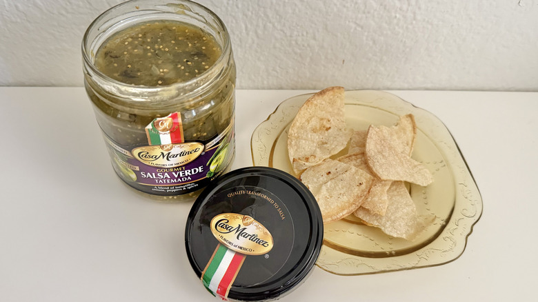 An open jar of Casa Martinez Salsa Verde Tatemada next to a bowl of tortilla chips