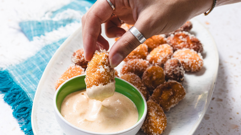 Hand dipping tater tot into sauce