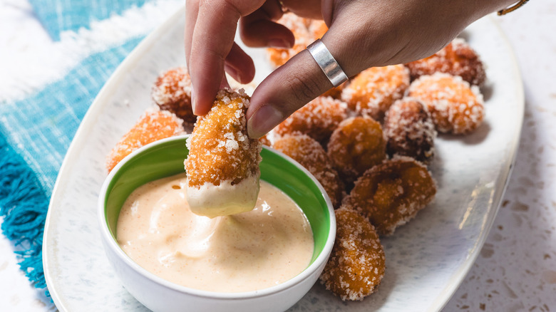 Hand dipping tater tot into sauce