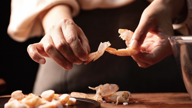 Hands peeling the tail off of a shrimp
