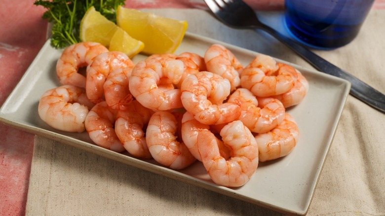 A plate of peeled shrimp garnished with lemon and parsley City on a cloth placemat next to a fork