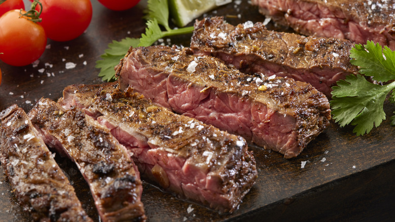 Close-up of sliced, medium-rare skirt steak next to herbs and tomatoes