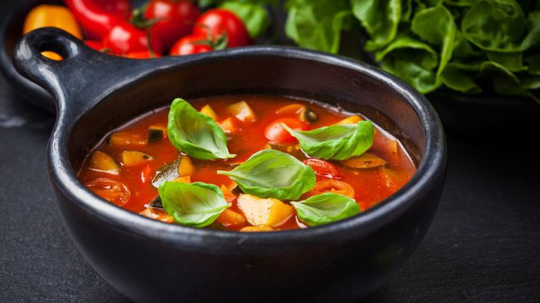 bowl of minestrone soup with tomatoes in background