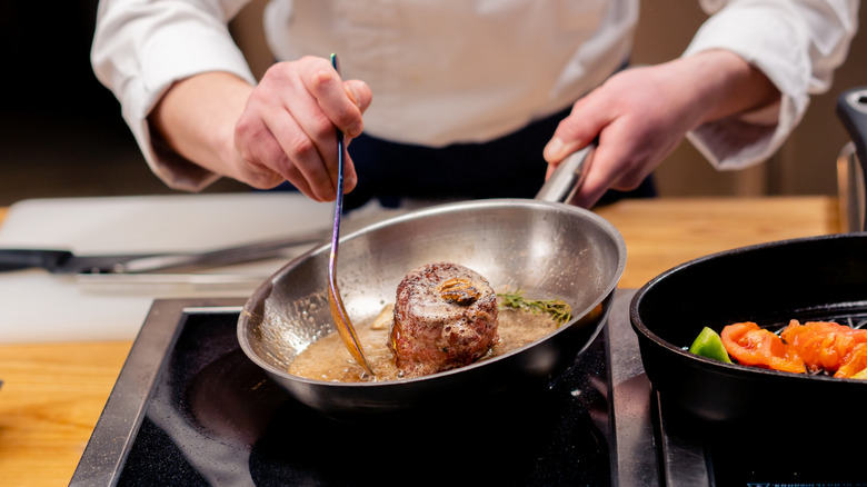 A chef spooning melted butter onto a steak being cooked in a pan