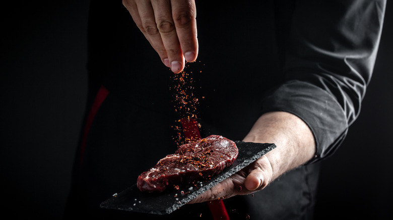 A hand sprinkling seasonings onto a steak