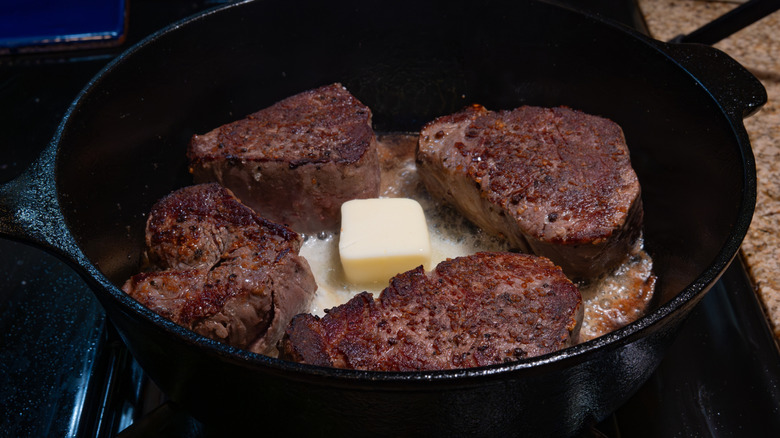 Four steaks cooking in a pan with a knob of butter in the middle
