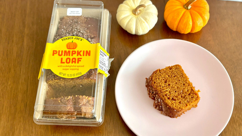 Trader Joe's pumpkin loaf slice on plate next to pumpkin loaf package and mini pumpkins