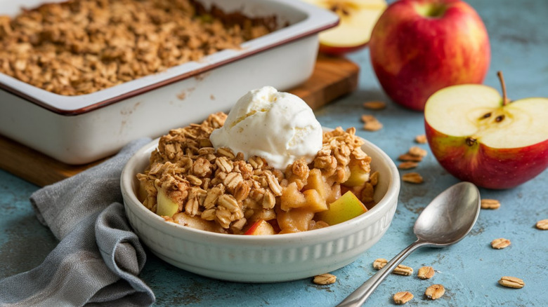 Freshly baked apple crisp in bowl next to apples
