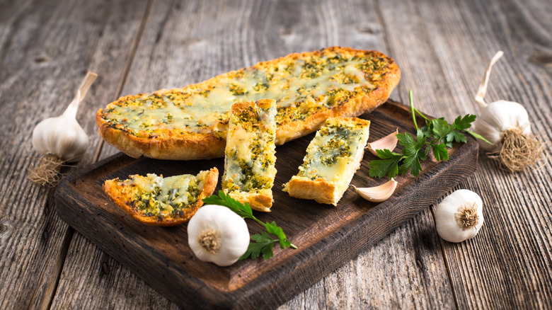 garlic bread with cheese and spices on a wood board