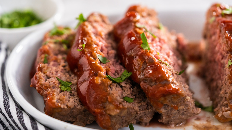 Juicy meatloaf with parsley and glaze on a white platter