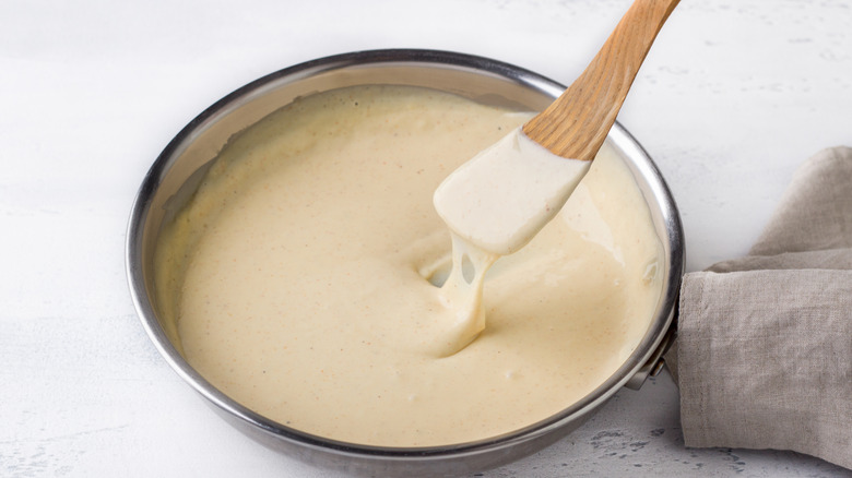 A spoon over a bowl of a light melted cheese sauce