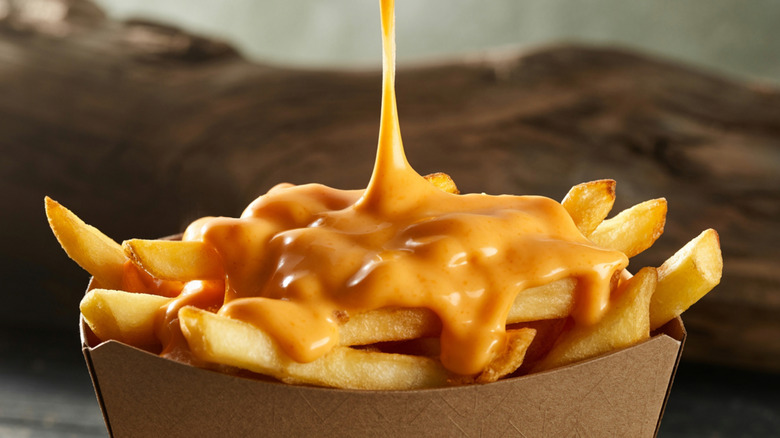 A melted cheese sauce being poured on a basket of fries