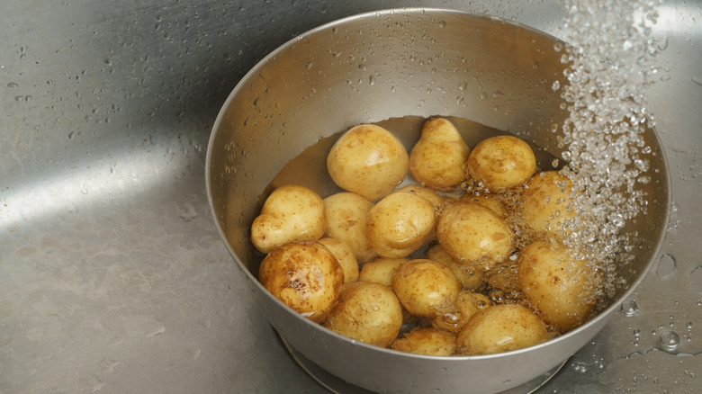 White potatoes soak in a water-filled bowl in a sink with running water.