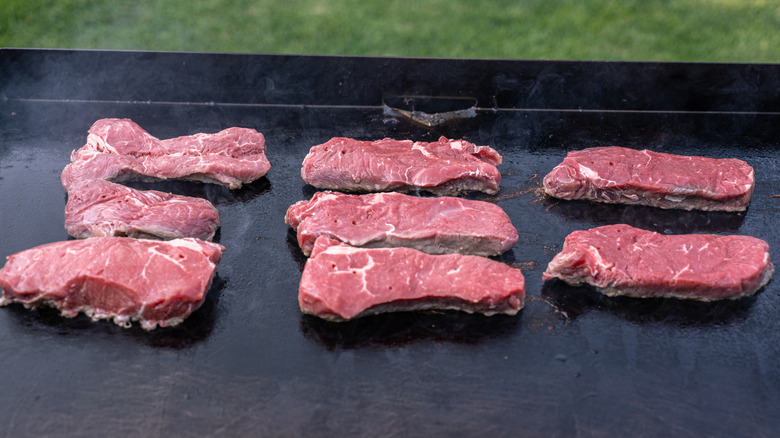 Several steaks start sizzling on a flat-top grill