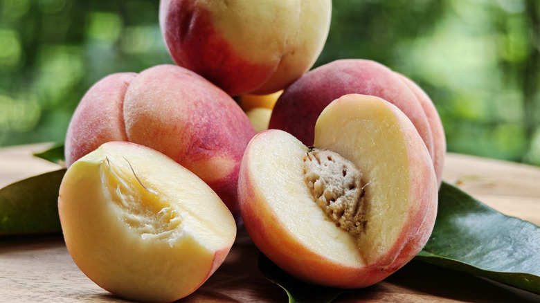 fresh peaches on an outdoor table with one cut open and a segment separated.
