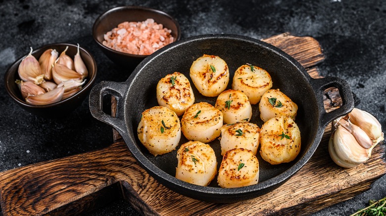Cooked scallops in a dish next to dishes of garlic and salt