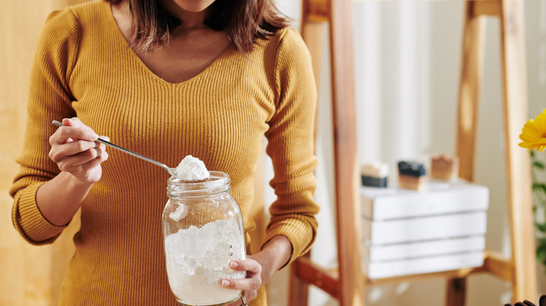 A woman taking a spoonful of baking soda from a jar
