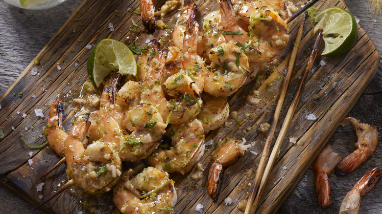 Tequila lime shrimp skewers on wooden board next to shrimp tails and lime wedge