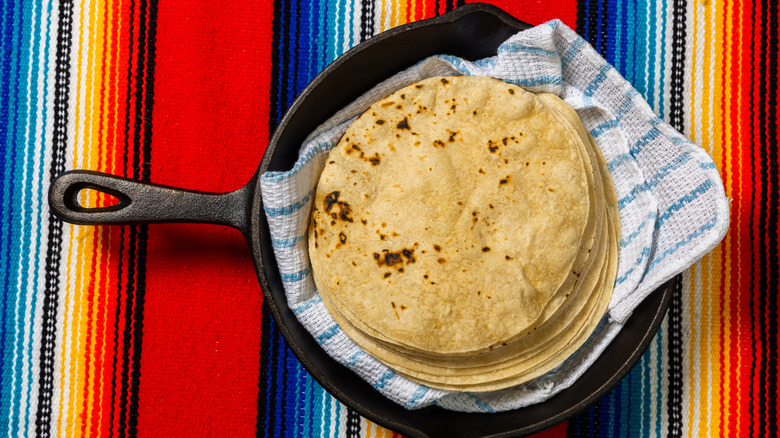 A cast iron skillet containing freshly warmed flour tortillas resting on a kitchen towel