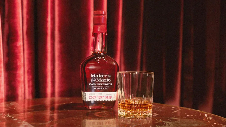 A bottle of Maker's Mark Cask Strength next to a poured glass in front of a red curtain