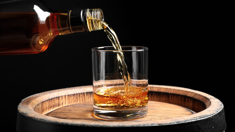 whiskey poured into glass atop barrel