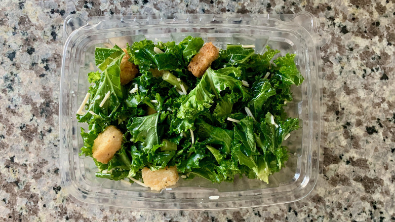 Whole Foods prepared garlicky kale salad in a plastic container on a stone surface