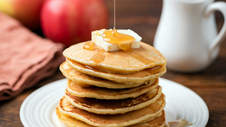 A stack of pancakes with a jar of milk in the background