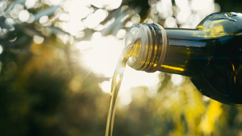 Olive oil poured from a bottle against a blurred sunny background