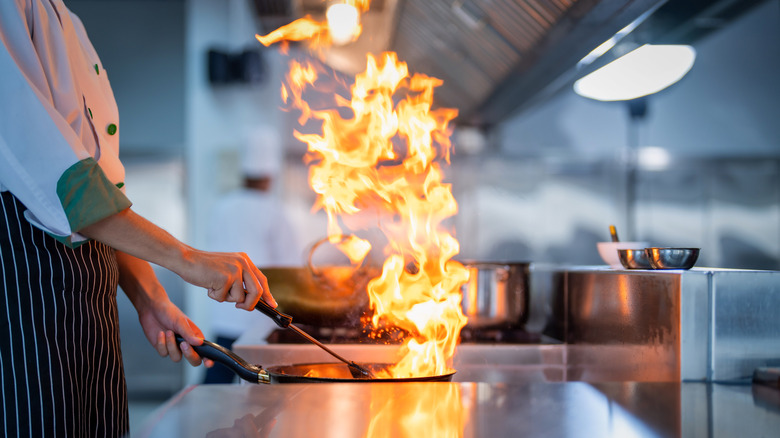 A cook manages a flaming pan