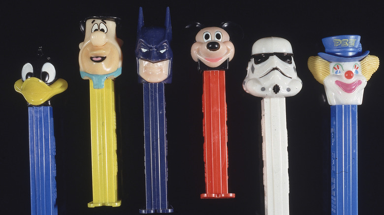 A line of Pez dispensers with character heads on top on a black background