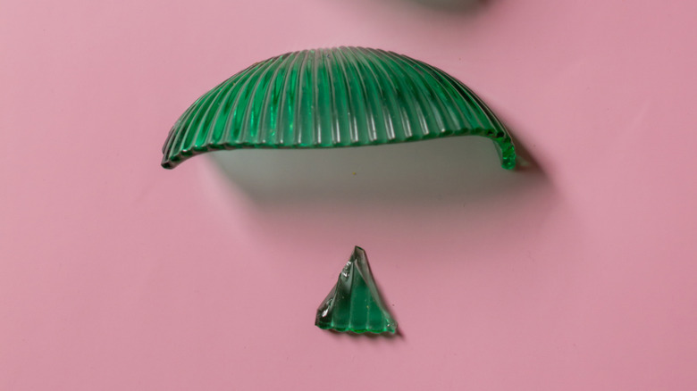 Two shards of a green glass bowl against a pink background