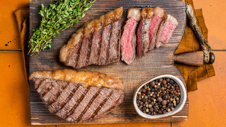 Two grilled picanha steaks on a cutting board with peppecorns and fresh herbs.