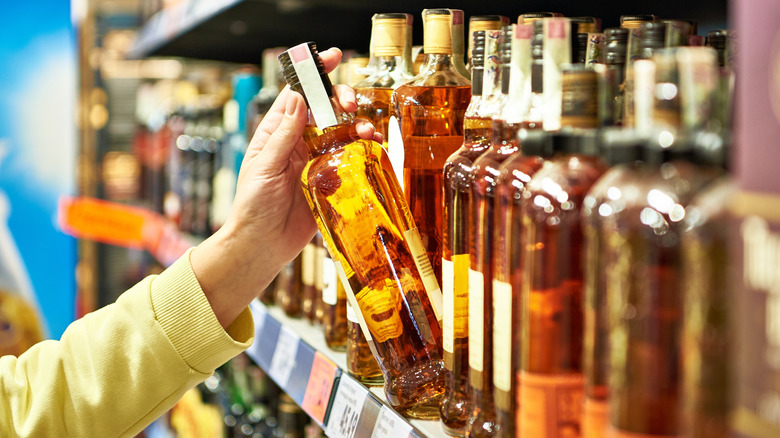 close up of a woman grabbing a bottle of whiskey from store shelf