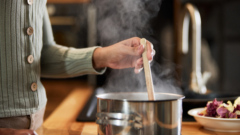 A person stirs a steamy saucepan with a wooden spoon