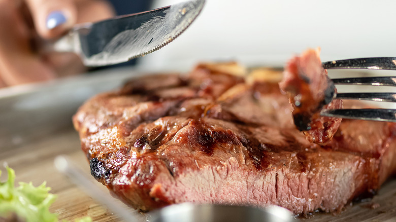 A woman holding a knife and fork, cutting a steak into a bite-sized piece
