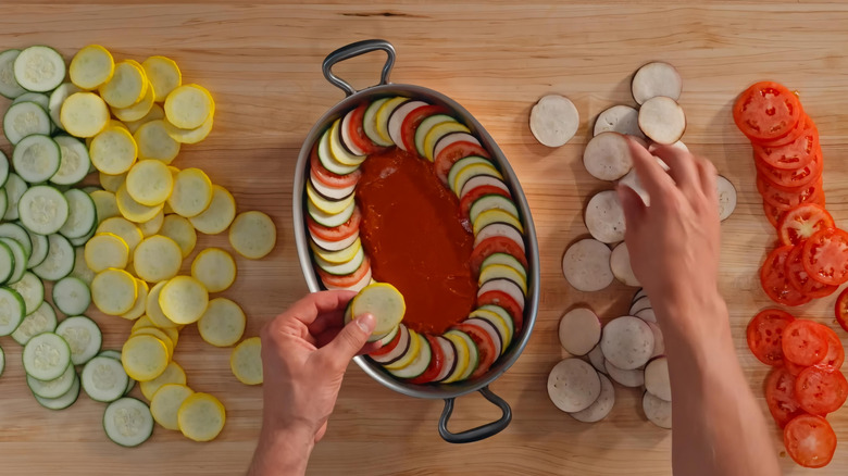 A person making ratatouille with thin coins of vegetable