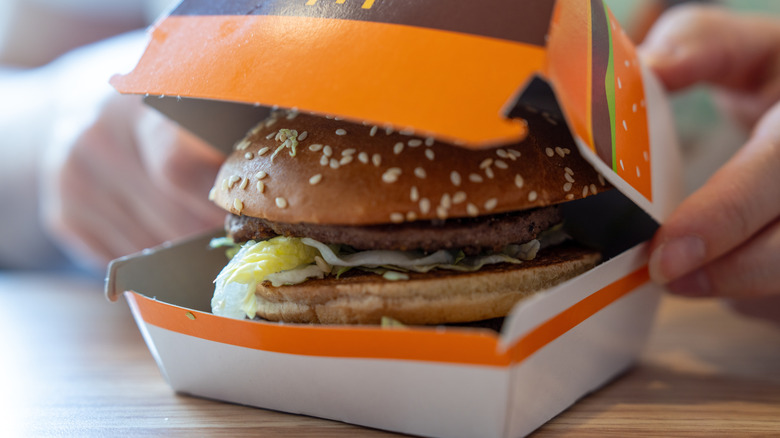 Hands opening a McDonalds burger box to reveal a sesame bun hamburger