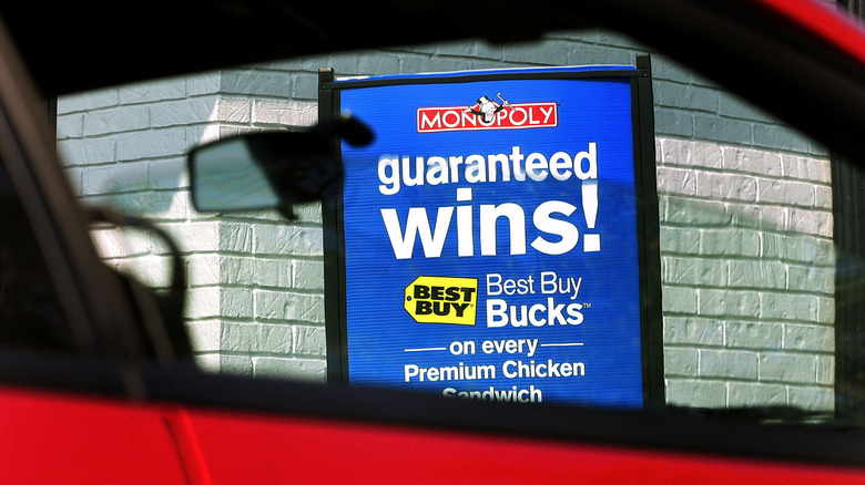 A sign for the new Monopoly game is framed in the window of a car in the drive-up lane of a McDonald's restaurant