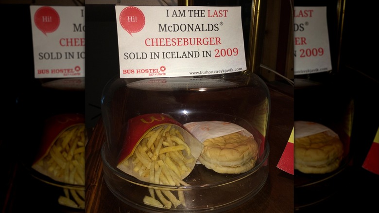 Mirrored image of a McDonald's burger in a glass case with a sign that says "I am the last McDonald's cheeseburger sold in iceland in 2009"