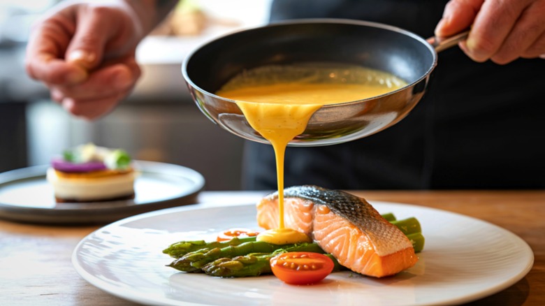 Chef pouring hollandaise sauce over a salmon filet