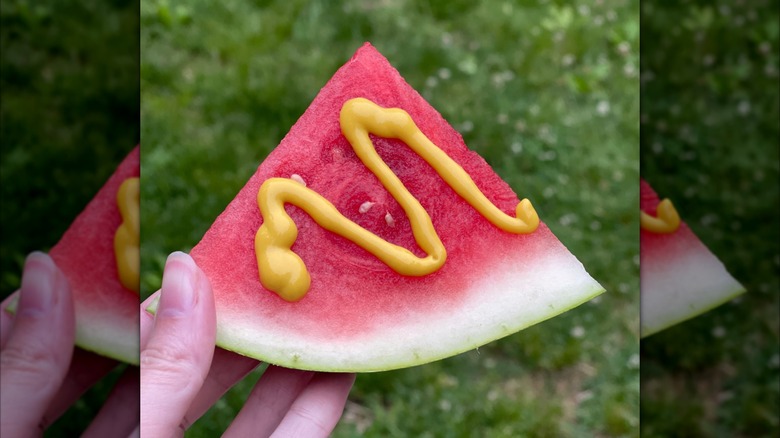 Foodie holding a slice of watermelon drizzled with mustard