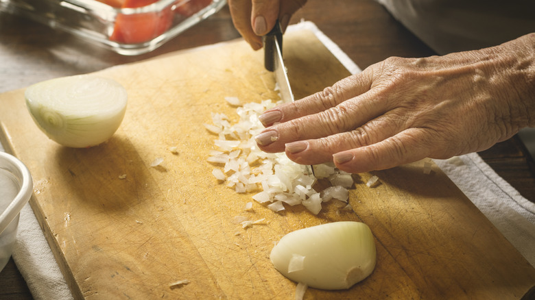 Hands chopping onions on wooden board